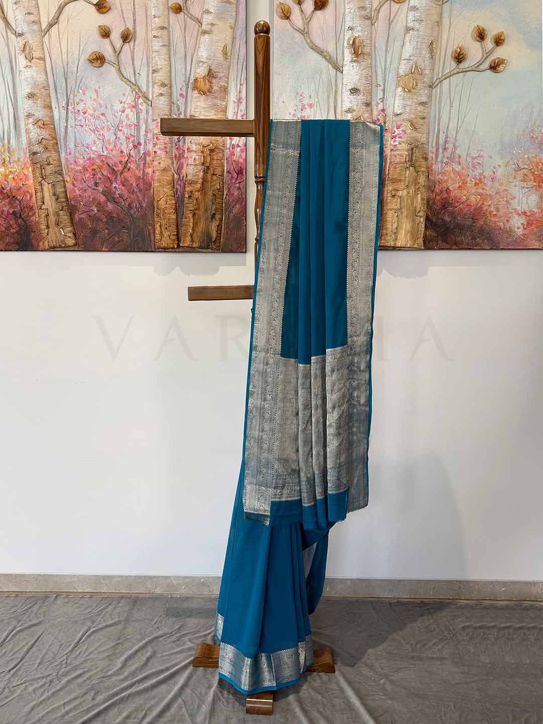 1️⃣ "A stunning Rama green georgette saree with delicate gold zari work, beautifully arranged on a wooden stand. The soft, flowing fabric drapes effortlessly, highlighting its luxurious feel and intricate detailing.