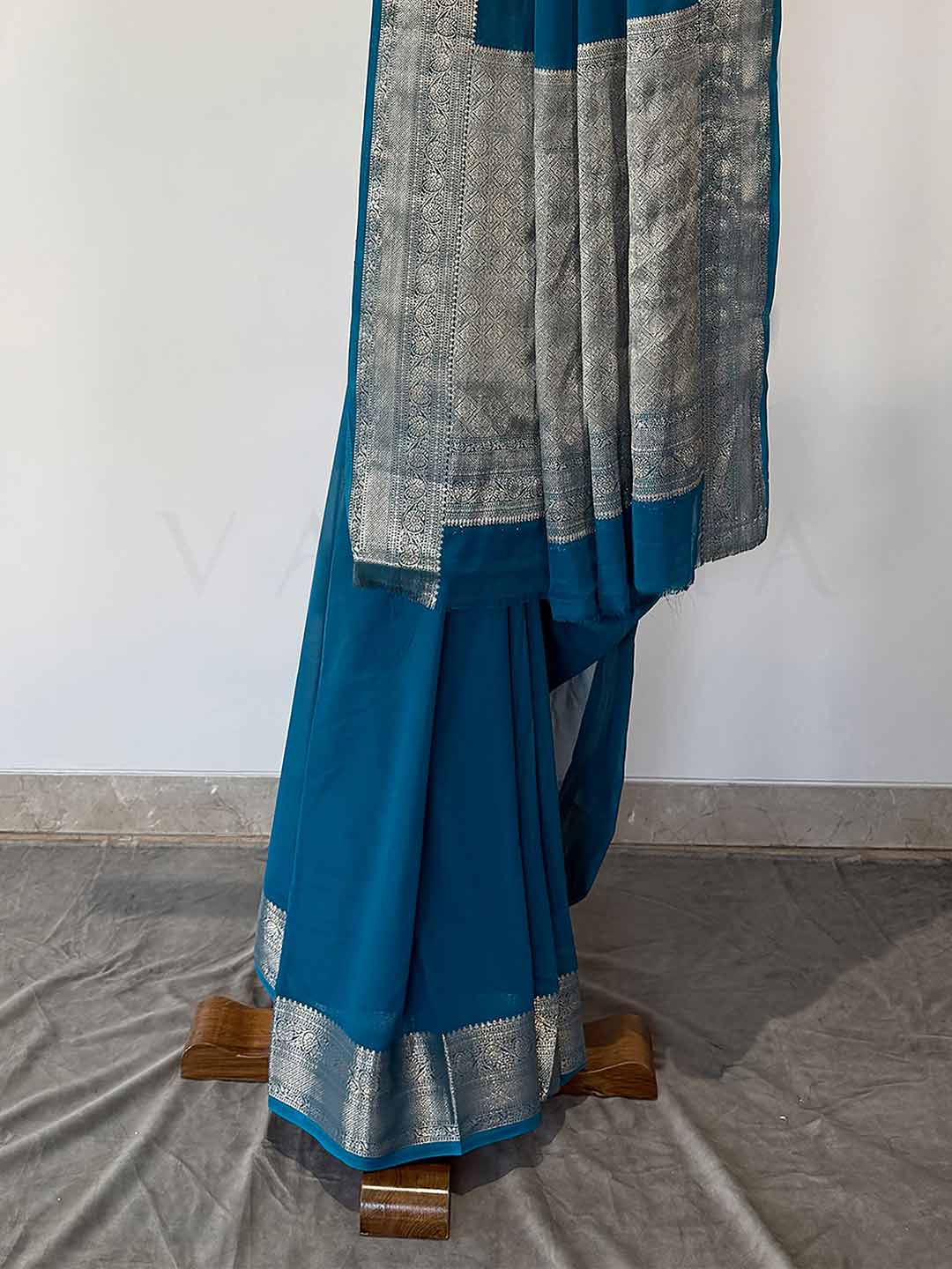 A rich Rama blue georgette saree adorned with intricate gold zari embroidery, draped artistically to emphasize its smooth texture and graceful fall. A striking piece for special occasions.