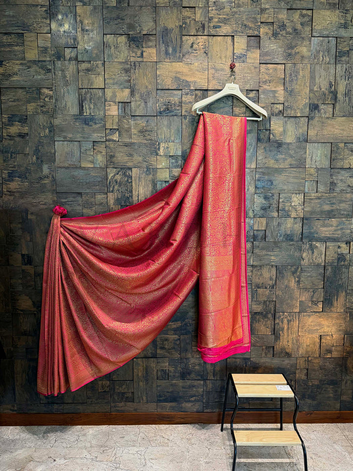 Red saree draped over a hanger against a textured wall. Full-length Mysore silk saree in rani pink with seamless zari detailing Premium viscose fabric Mysore saree styled for traditional occasions
