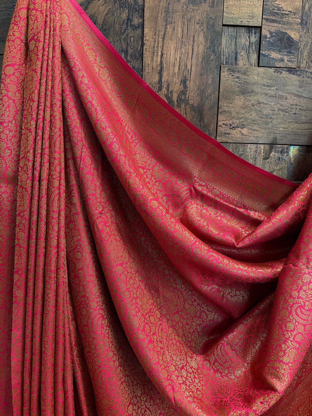 Decorative green fabric with intricate embroidery on a wooden stand against a textured wall. Unstitched blouse piece with matching zari weave in Mysore silk saree with Front pleat detailing of all-over woven zari work on rich pink silk saree