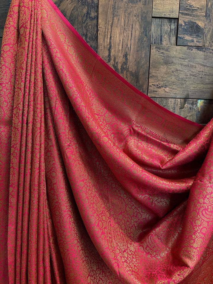 Decorative green fabric with intricate embroidery on a wooden stand against a textured wall. Unstitched blouse piece with matching zari weave in Mysore silk saree with Front pleat detailing of all-over woven zari work on rich pink silk saree