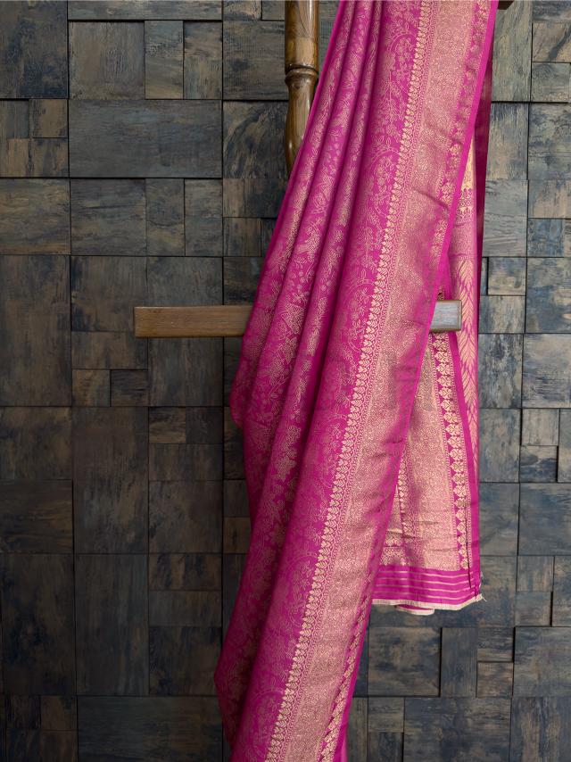 Blouse piece in rani pink with golden zari floral designs - unstitched and crafted for regal ethnic wear. - Silk texture captured in light to showcase the brilliance of zari weaving over rani pink kanjivaram drape