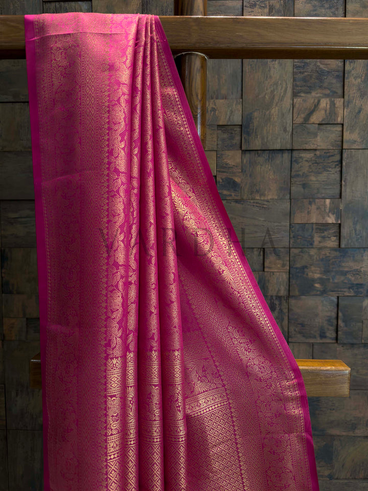 Close-up of rani pink saree body showing dense gold zari floral jaal and slim selvedge, lustrous art silk texture for celebrations