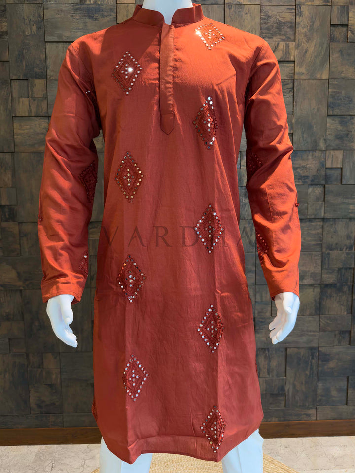 Orange embroidered kurta on a mannequin against a wooden paneled wall. Front panel detail of men’s viscose kurta featuring evenly spaced mirror work butis, tonal thread accents and a soft fabric sheen.