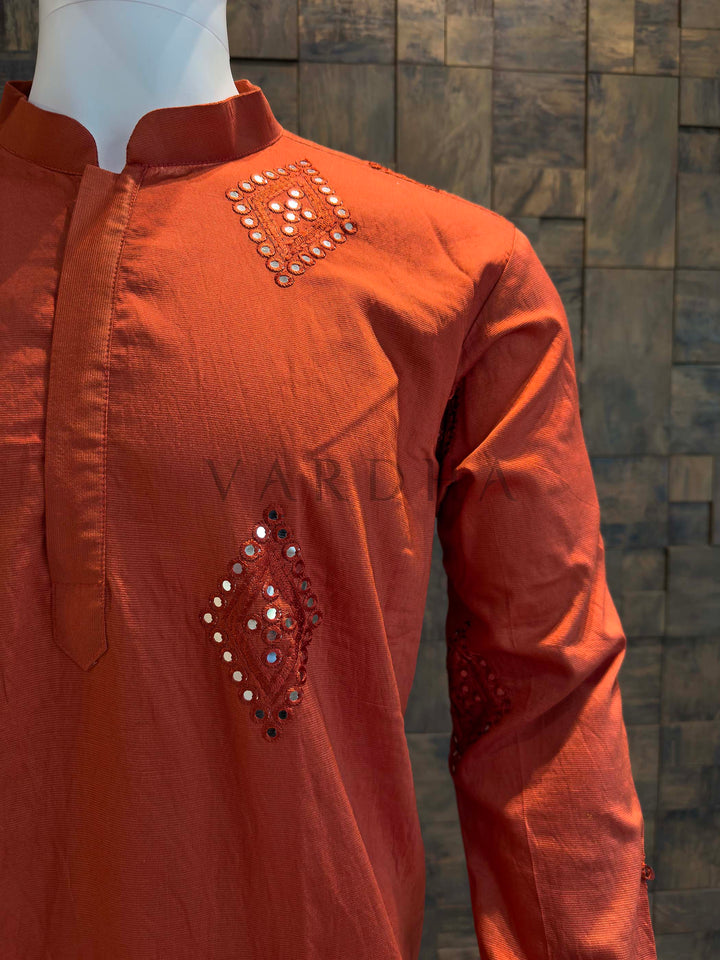 Orange kurta with intricate beadwork on a mannequin against a textured wall. Angle shot highlighting concealed placket construction, crisp collar and symmetrical placement of mirror butis across chest and sleeves.