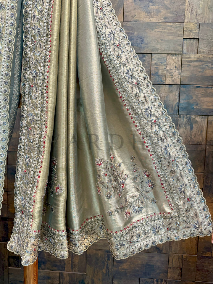 Silk saree with intricate embroidery on a wooden background. Close-up of pallu showing delicate cutdana, stone, and thread embroidery on shimmer base.
