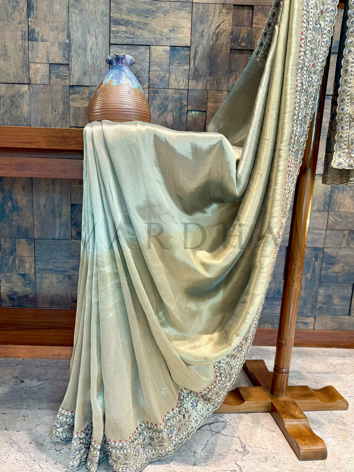 Light green fabric draped over a wooden stand against a wooden paneled wall. saree showing full pallu with floral hand embroidery and sequin patterns.