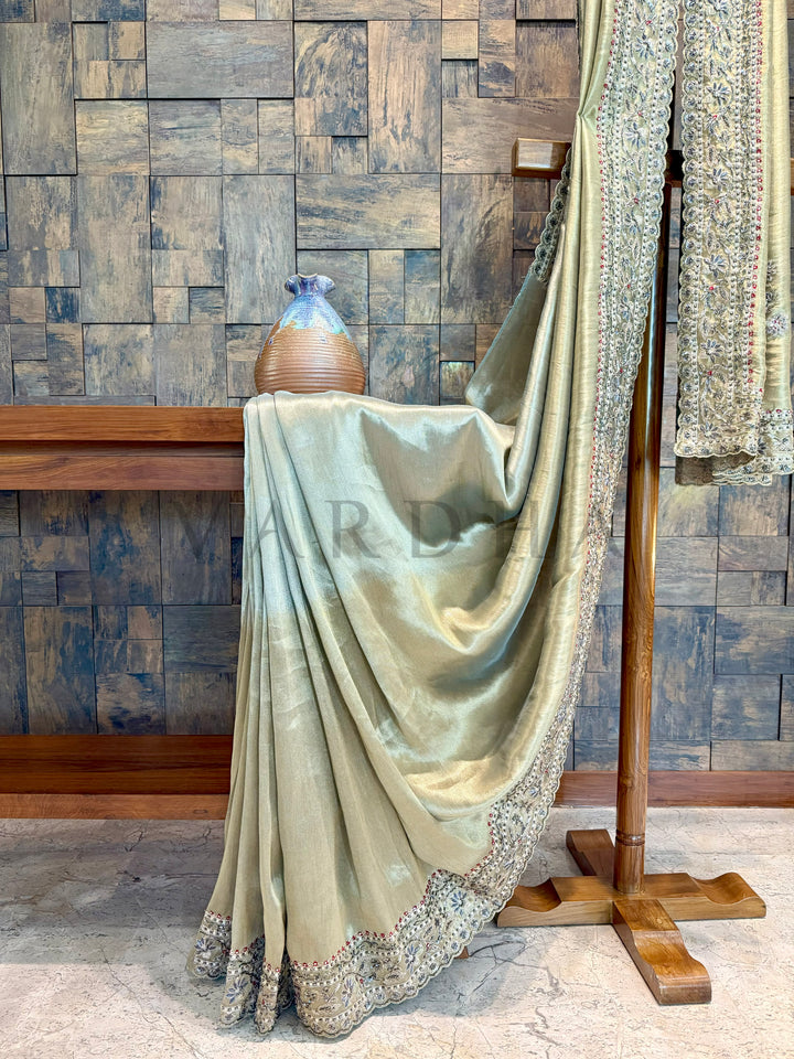 Green saree with silver border draped over a wooden stand against a wooden paneled wall. sage green saree styled with classic gold jewelry for ethnic occasions.