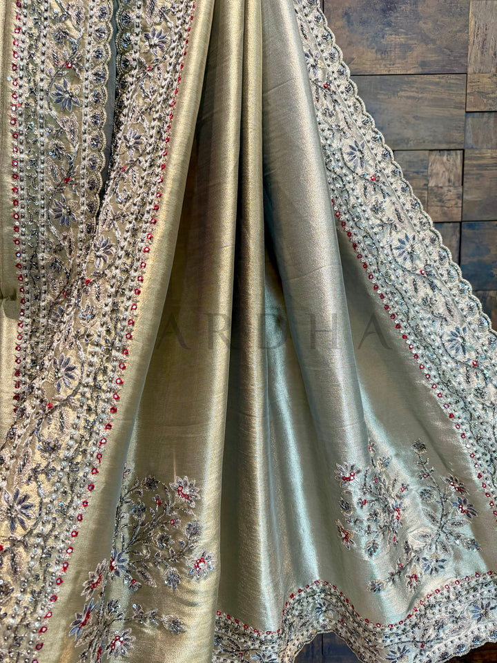 Silk fabric with intricate embroidery on a wooden surface. Border detail of the saree with fine beadwork and floral thread motifs on light green base.