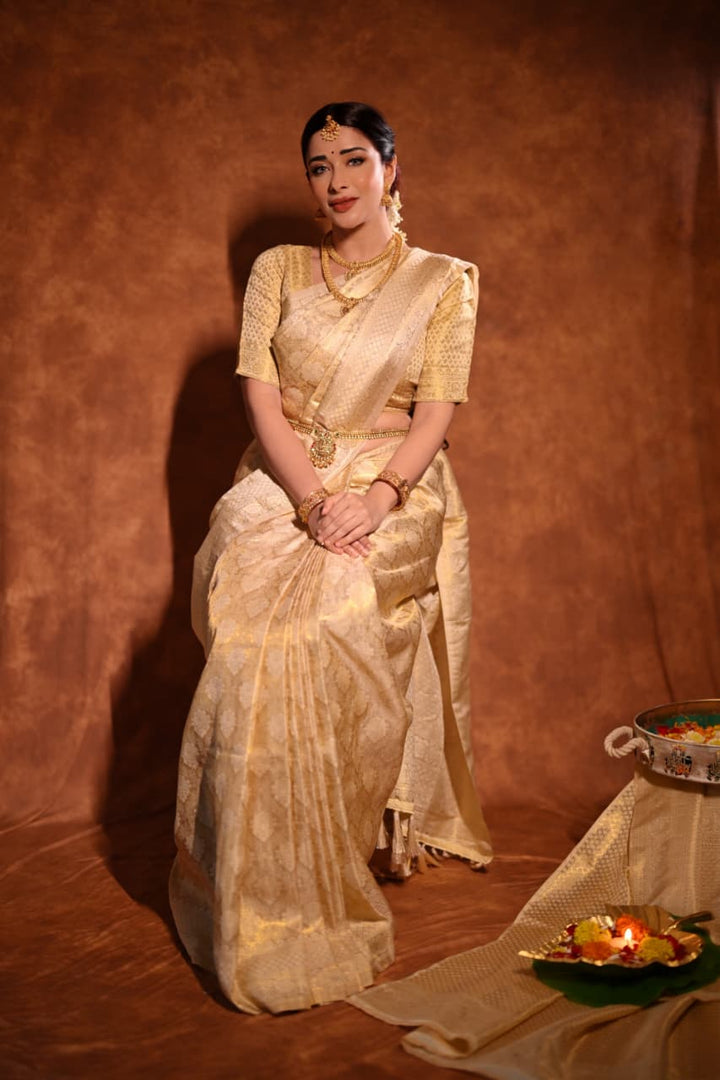Nyra Banerjee in a traditional gold kanjivaram silk saree sitting on the floor with a brown background