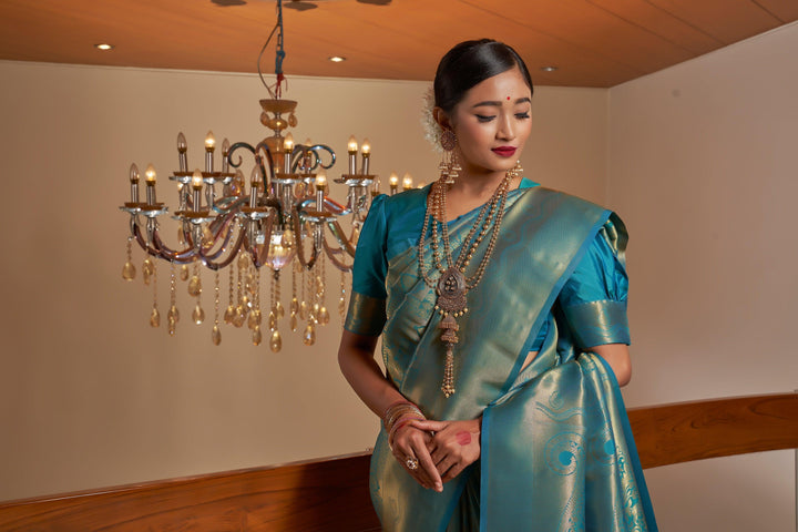 Flat lay of the saree and blouse piece, highlighting the rich teal blue silk texture and craftsmanship.