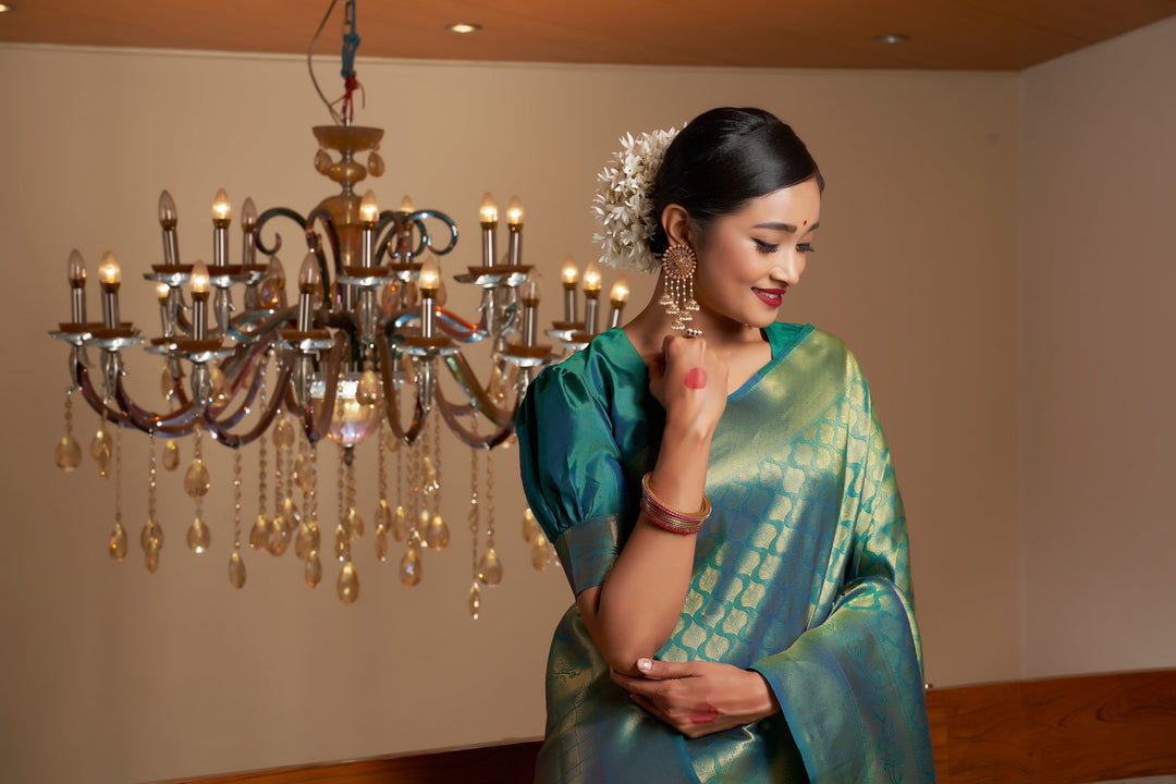 Flat lay image displaying the saree and blouse piece in pine green silk with gold detailing.