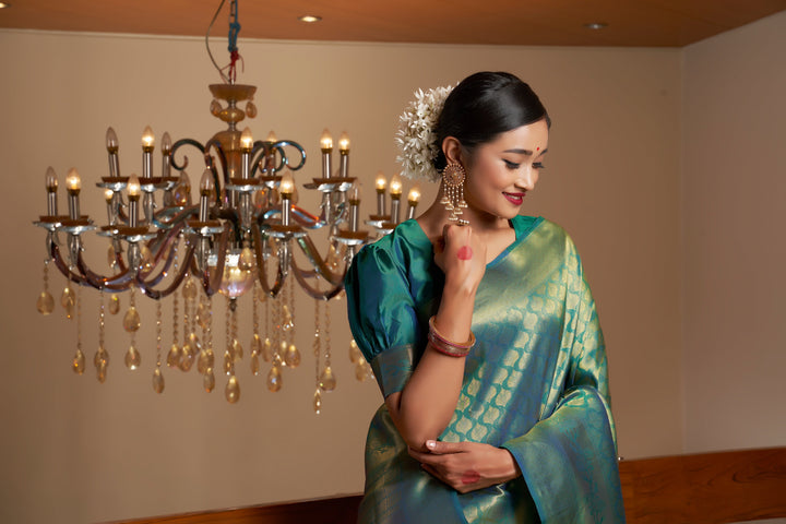 Flat lay image displaying the saree and blouse piece in pine green silk with gold detailing.