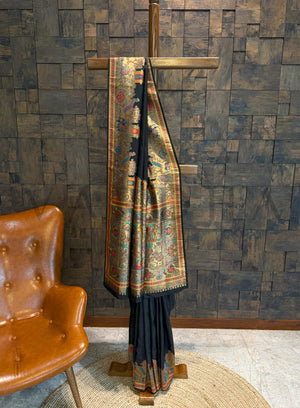 Saree draped over a wooden stand against a textured wall with a brown chair.