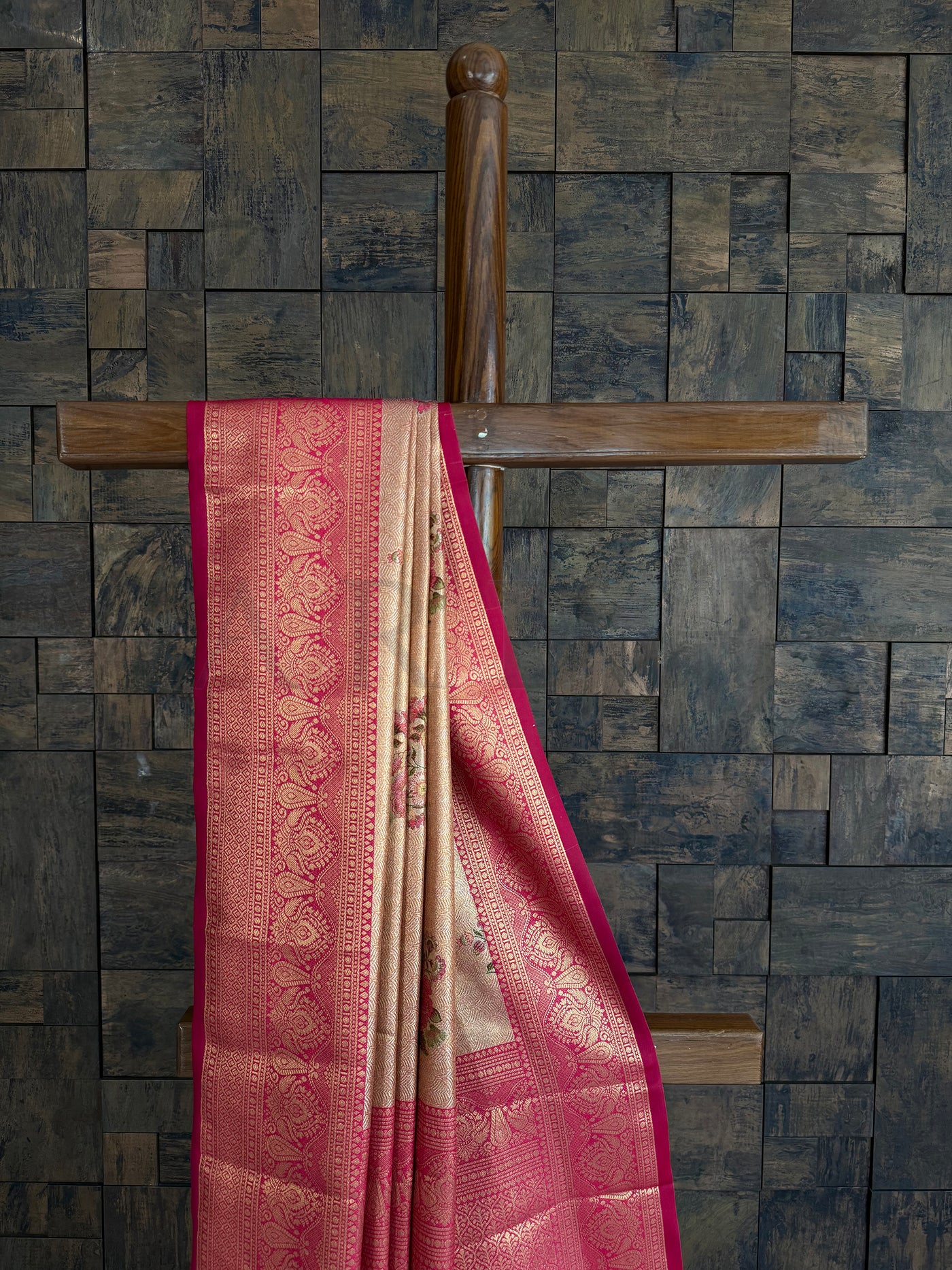 Kanjivaram saree with pink and gold patterns draped over a wooden rod against a textured wall.