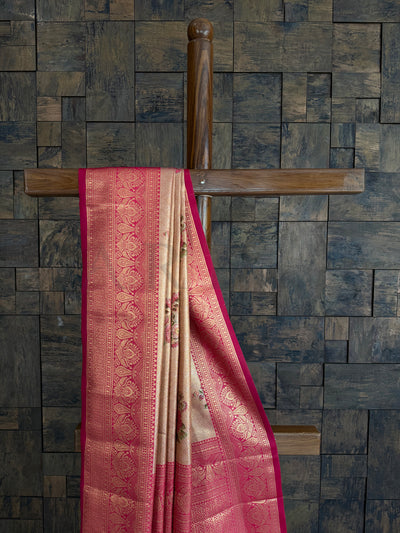 Kanjivaram saree with pink and gold patterns draped over a wooden rod against a textured wall.