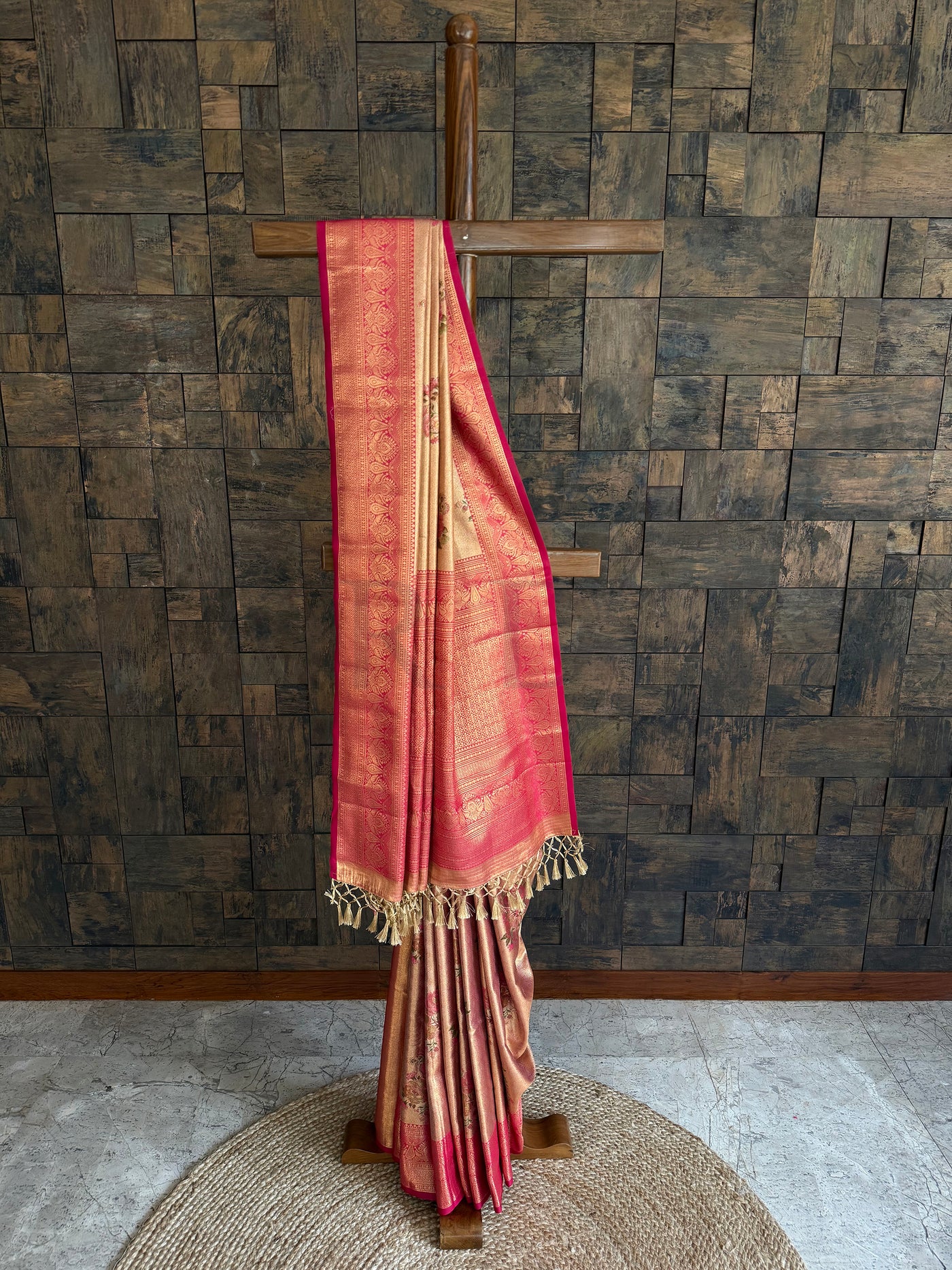 Beige saree with gold border on a wooden stand against a textured wall.
