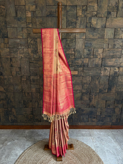 Beige saree with gold border on a wooden stand against a textured wall.