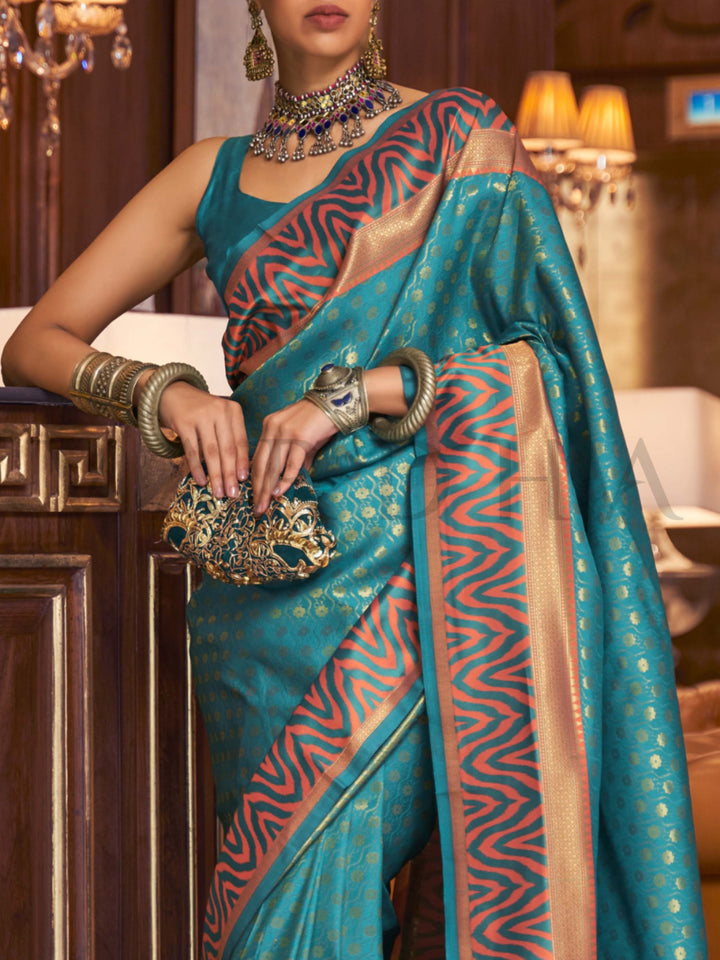 This luxurious Teal Blue–Copper Kanjivaram Silk saree features classic woven zari work with contrast pallu and ornate detailing. Elegant wedding attire with heritage style and timeless drape. SKU 271001. This luxurious Teal Blue–Copper Kanjivaram Silk saree features classic woven zari work with contrast pallu and ornate detailing. Elegant wedding attire with heritage style and timeless drape. SKU 271001.