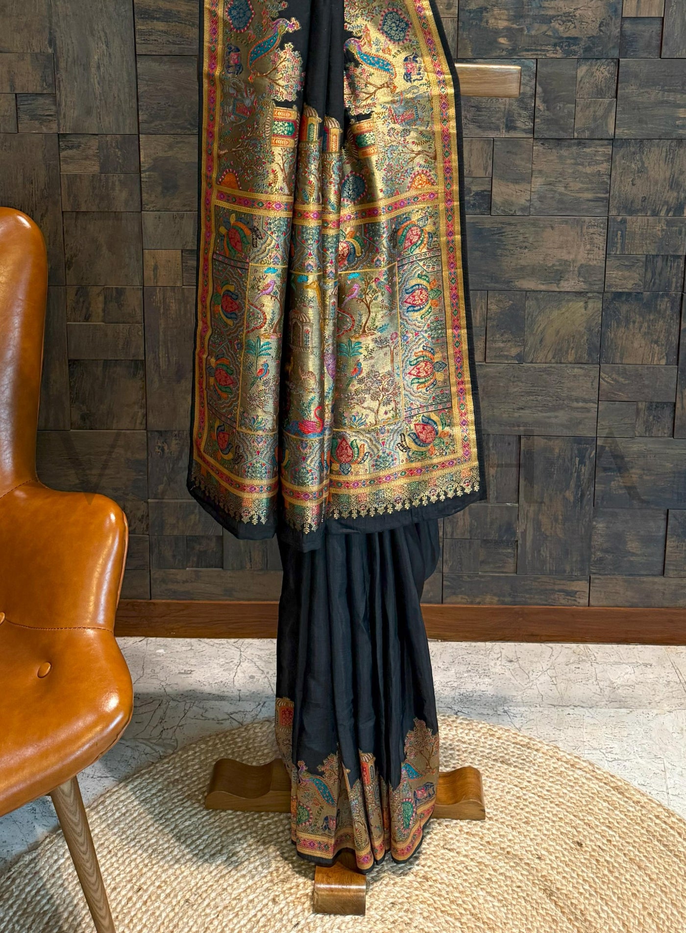 Traditional black saree with a colorful border draped over a chair against a wooden paneled wall.