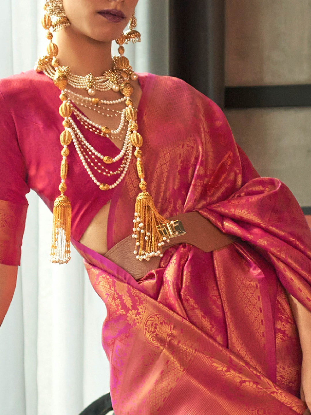 Classic kanjivaram wedding saree in magenta rose hues, styled with gold accessories. Traditional silk saree in rose pink and magenta with heavy golden zari weaving and pallu tassels.