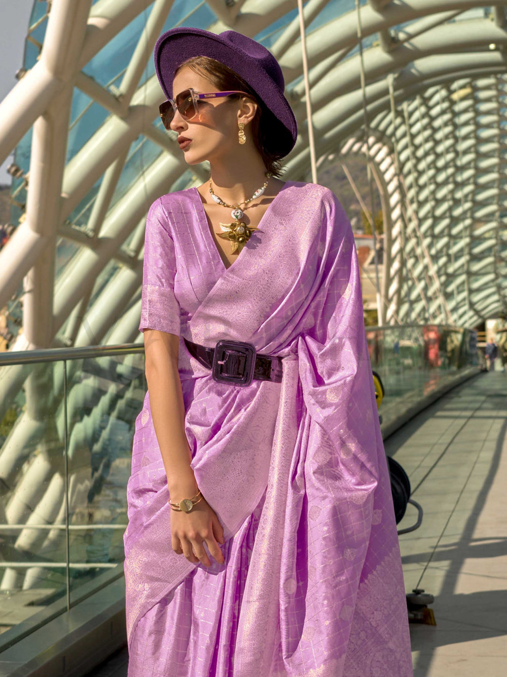 Orchid Mauve Katan silk saree with Ivory Zari zari detailing, featuring checks handloom weaving, designer blouse and tasselled pallu — a perfect fit for sangeet and designer cocktail. Styled with modern belts, hats, and accessories to blend heritage and couture elegance. This image captures the side angle view showcasing blouse styling and zari border detail, ideal for visualizing festive elegance, designer appeal, and modern styling inspiration. Perfect for online shoppers seeking detailed previews before 