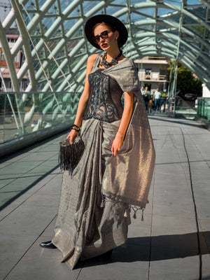 Champagne Grey Katan silk saree with Matte Silver zari detailing, featuring checks handloom weaving, designer blouse and tasselled pallu — a perfect fit for bollywood and award nights. Styled with modern belts, hats, and accessories to blend heritage and couture elegance. This image captures the front drape view highlighting pallu fall and pleats alignment, ideal for visualizing festive elegance, designer appeal, and modern styling inspiration. Perfect for online shoppers seeking detailed previews before pu