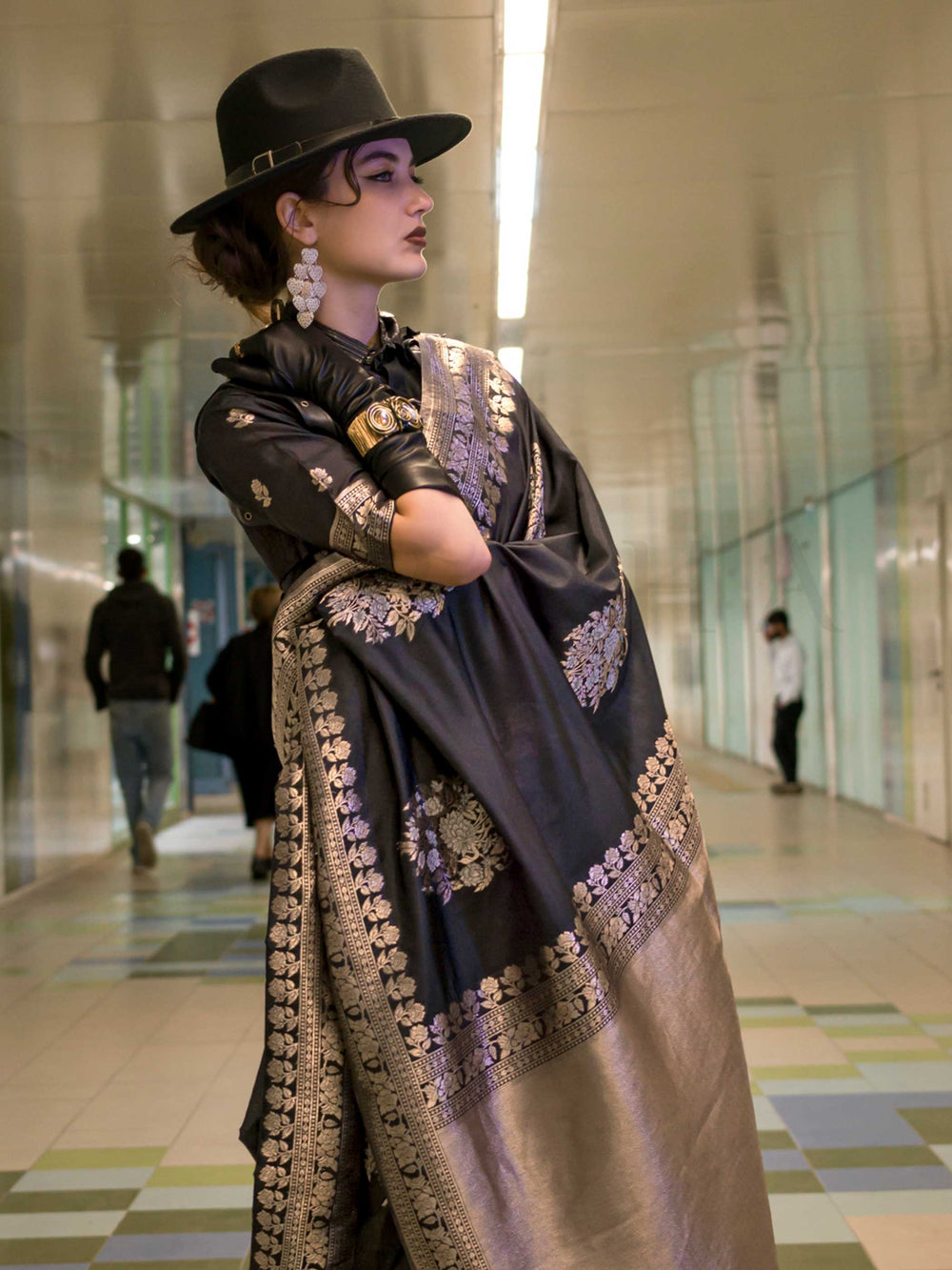 Jet Black silk saree with Old Gold Zari zari and Antique Beige floral motifs, styled with contrast blouse, handloom weaving, festive-ready look with cinematic silhouette and bold accessories — ideal for events and grand celebrations. This image captures the side angle view showcasing blouse styling and zari border detail, ideal for visualizing festive elegance, designer appeal, and modern styling inspiration. Perfect for online shoppers seeking detailed previews before purchase, enhancing saree visual merch