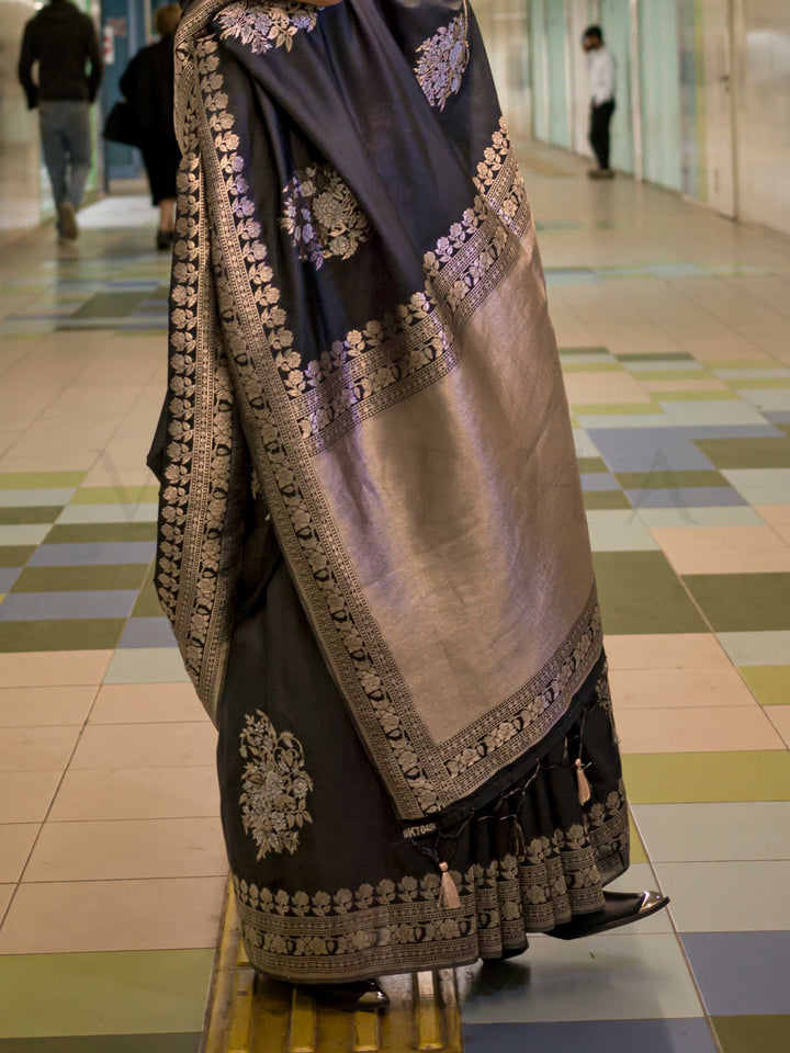 Jet Black silk saree with Old Gold Zari zari and Antique Beige floral motifs, styled with contrast blouse, handloom weaving, festive-ready look with cinematic silhouette and bold accessories — ideal for events and grand celebrations. This image captures the back drape focus revealing pallu finesse and motif richness, ideal for visualizing festive elegance, designer appeal, and modern styling inspiration. Perfect for online shoppers seeking detailed previews before purchase, enhancing saree visual merchandis