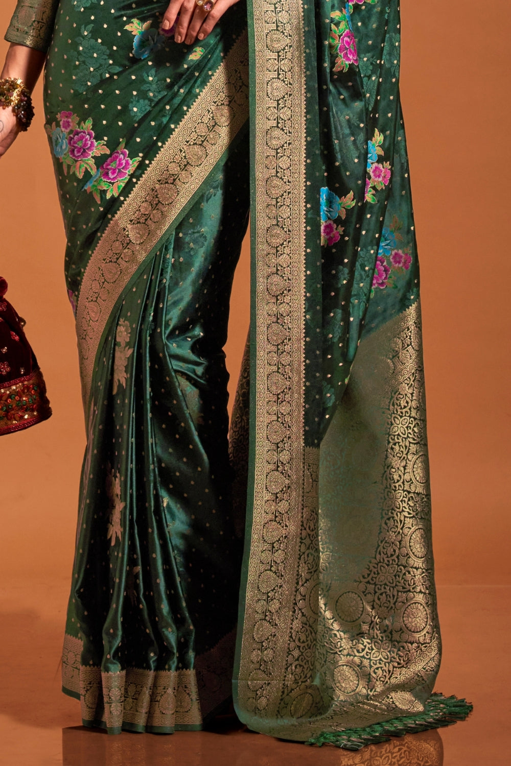 Bottle Green pure satin silk saree with multicolour floral handloom weaving and rich zari border. Styled for sangeet and perfect for evening bride entry, blending regal silk elegance with festive florals. This image captures the side angle view showcasing blouse styling and zari border detail, ideal for visualizing festive elegance, designer appeal, and modern styling inspiration. Perfect for online shoppers seeking detailed previews before purchase, enhancing saree visual merchandising and SEO-rich product