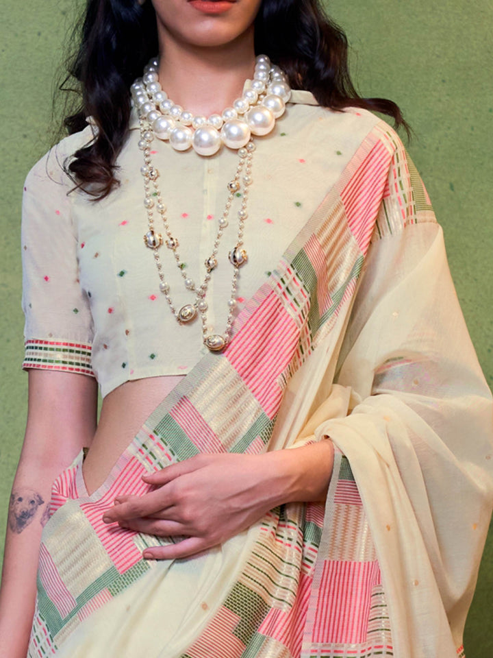 Subtle Ivory–Pink cotton saree styled with check borders and artisan-inspired floral pallu. Ivory–Pink soft spun saree with handwoven detailing across pallu and border, festive ready.