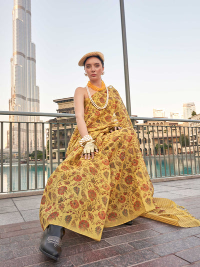 Yellow and Burnt Orange zari tissue saree with printed floral motifs and zari pallu This image captures the model styling perspective with complete saree ensemble displayed, ideal for visualizing festive elegance, designer appeal, and modern styling inspiration. Perfect for online shoppers seeking detailed previews before purchase, enhancing saree visual merchandising and SEO-rich product display strategy.                                                                                                       