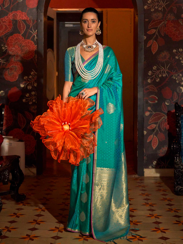 Teal Blue–Gold banarasi satin silk saree with rich woven zari work and golden pallu styled for weddings. Model in Teal Blue–Gold silk saree featuring temple-inspired zari buta and traditional border..