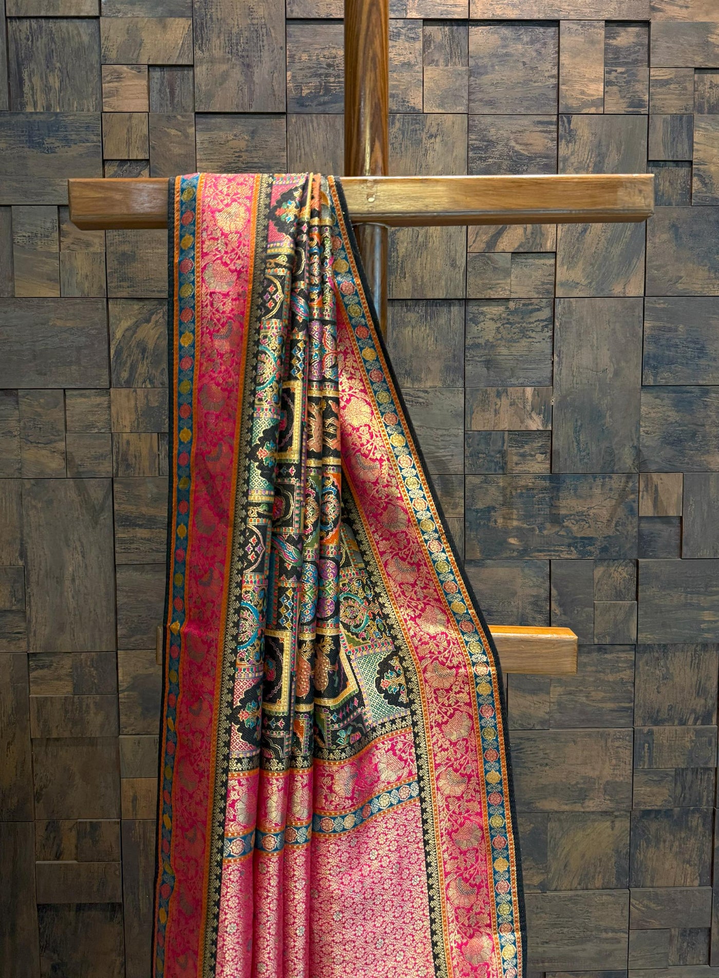 Colorful patterned saree draped over a wooden cross against a textured wall.