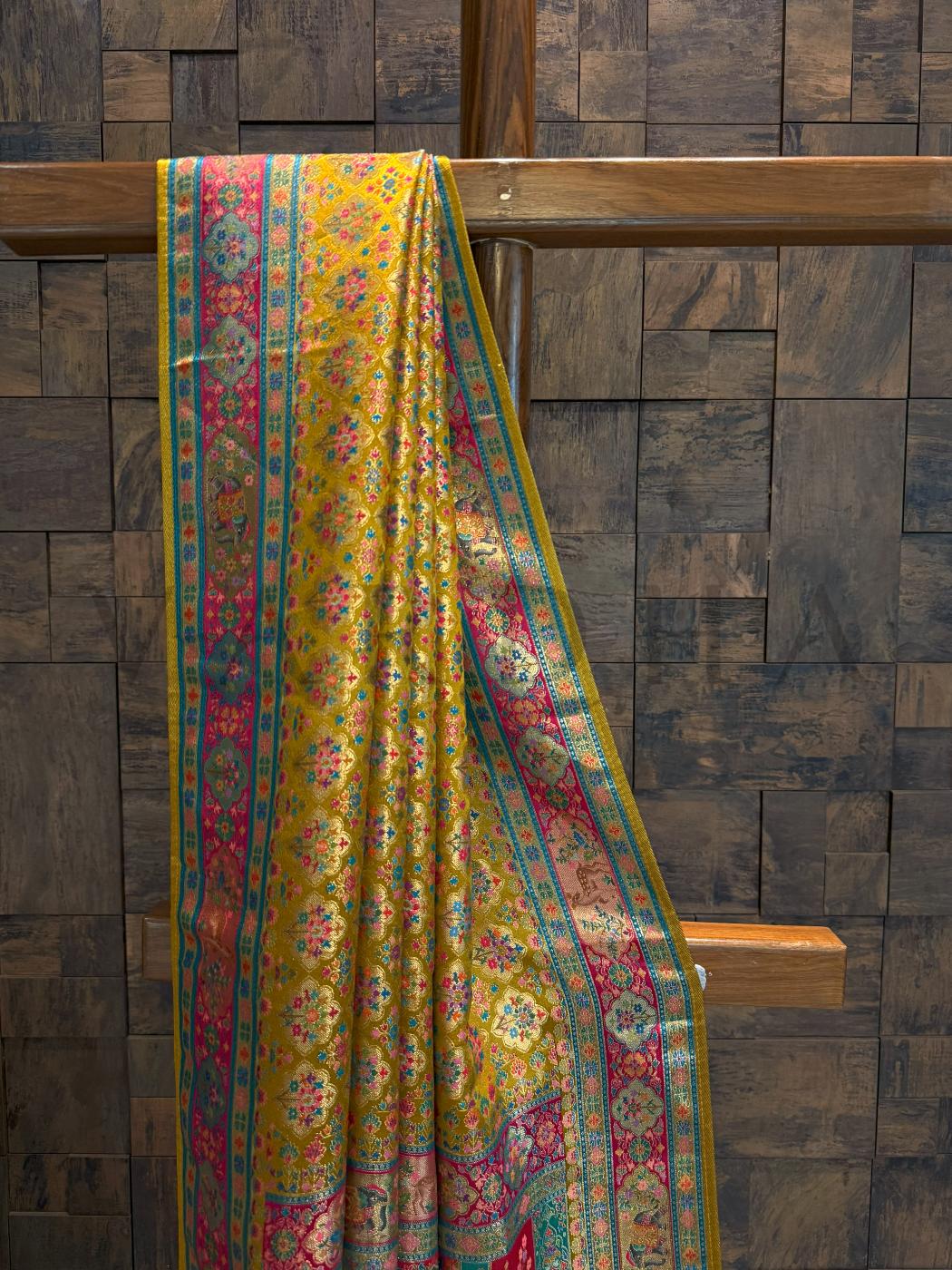 Colorful patterned fabric draped over a wooden rod against a wooden paneled wall.