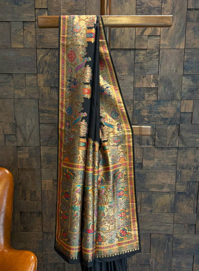 Saree with intricate patterns hanging on a wooden rod against a textured wall.