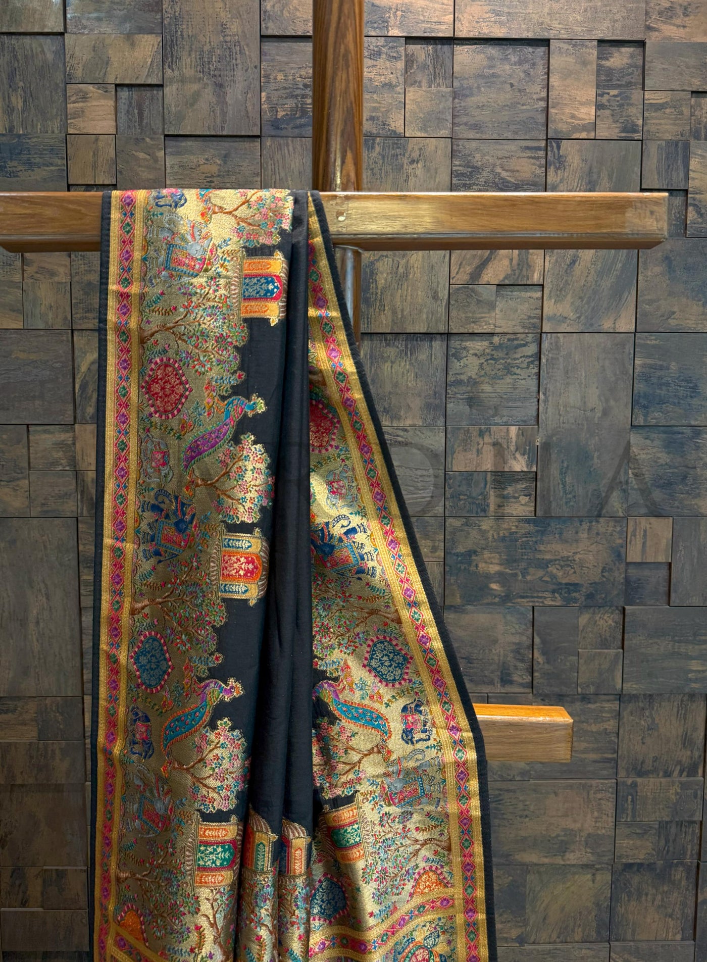 Colorful saree draped over a wooden rod against a wooden paneled wall.