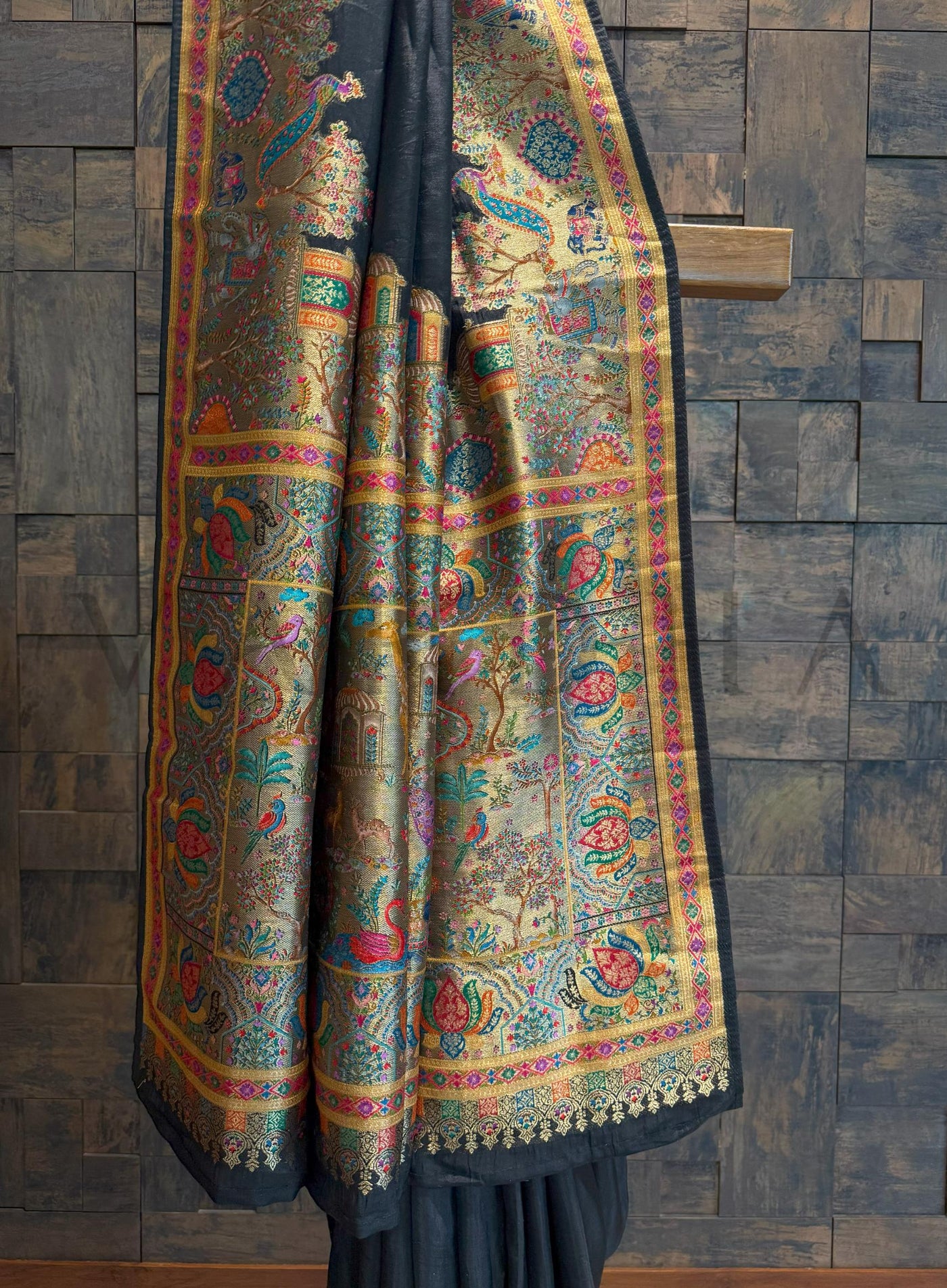 Colorful black saree draped over a wooden surface against a stone wall background