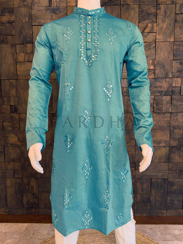 Teal embroidered kurta on a mannequin against a wooden paneled wall. Front panel of men’s aqua kurta highlighting geometric mirror motifs and tonal thread accents on smooth viscose fabric with gentle sheen.