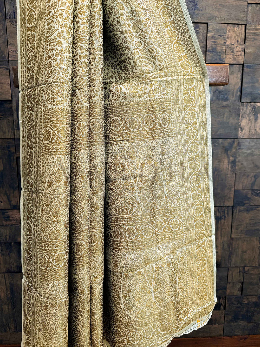 Decorative fabric with intricate patterns draped over a wooden surface Close-up of the pallu showing rich gold zari jaal work in Mysore silk fabric with elegant sheen.