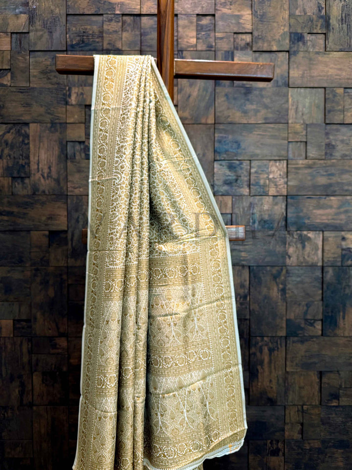 Green patterned towel hanging on a wooden rack against a wooden paneled wall. Saree hanging elegantly to show fluid drape, sheen, and traditional Mysore weaving craftsmanship.
