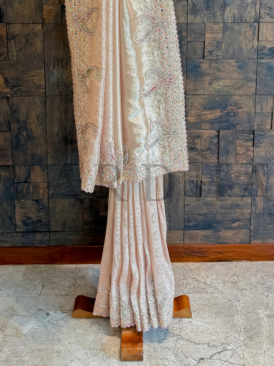 Lace dress on a wooden stand against a textured wall. Detailed image of shimmering mirror work and cutdana accents on pink tissue silk saree
