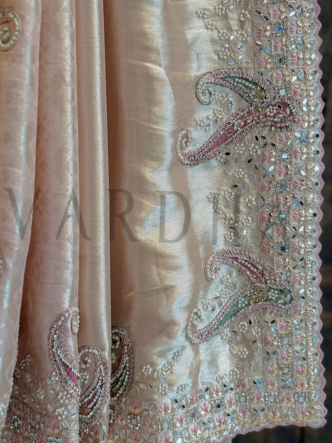 Decorative fabric with intricate beadwork and embroidery, featuring the brand 'Vardha'. Designer pink silk saree pleats with woven geometric motifs and zari detailing