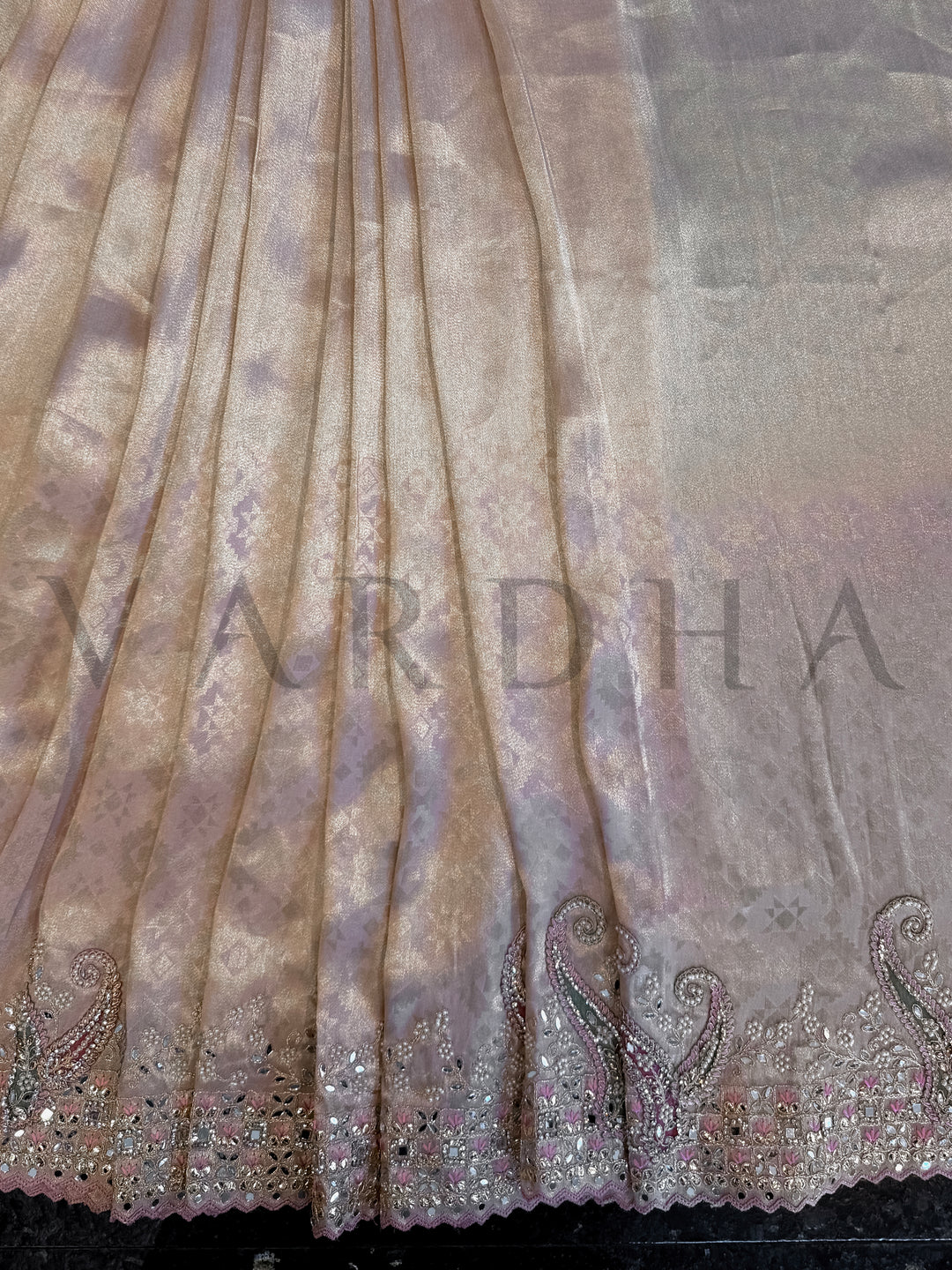 Close-up of a fabric with intricate patterns and 'Vardha' branding. Border shot showing intricate stone and mirror grid work in blush, silver, and green