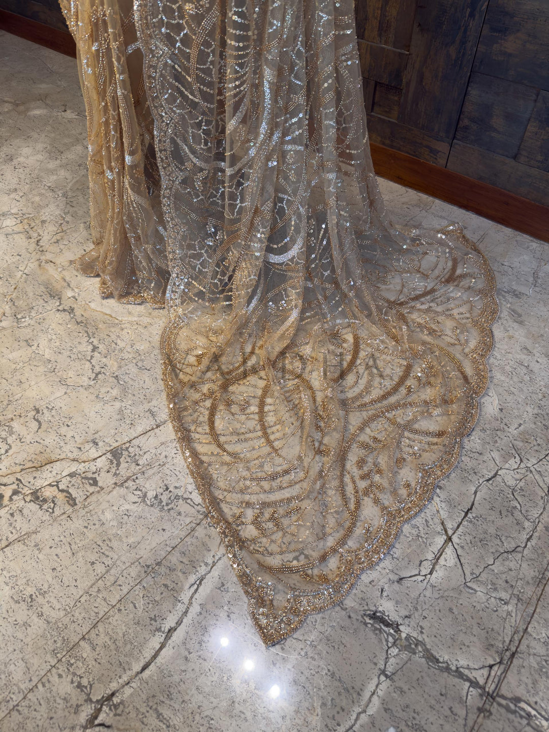 Decorative fabric with intricate patterns on a marble floor Luxurious Beige festive Net Saree from House of Vardha featuring radiant bead and sequin work, perfect for glamorous evening parties and receptions. We offer Ready to wear, Pre drape service, Saree Add on, Custom Stitched Blouse, Fall and Edging, Gift Packaging at Complimentary Price!