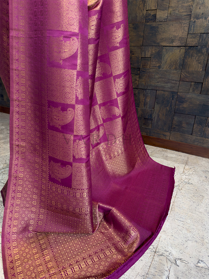 Magenta saree with intricate patterns on a wooden floor and wall. Luxurious Indian wedding saree in a rich purple hue from House of Vardha with heavy gold zari embellishments. designer berry purple silk saree with traditional gold weaving, ideal for bridal and ethnic occasion wear.