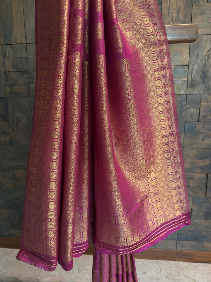 Purple saree with gold patterns draped over a wooden chair against a stone wall.