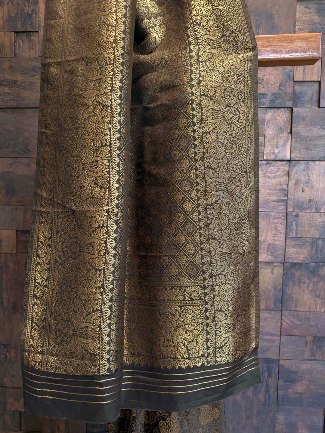 Traditional patterned fabric draped over a wooden surface. Close-up of zari-woven peacock motifs on Black traditional art silk saree for festive wear