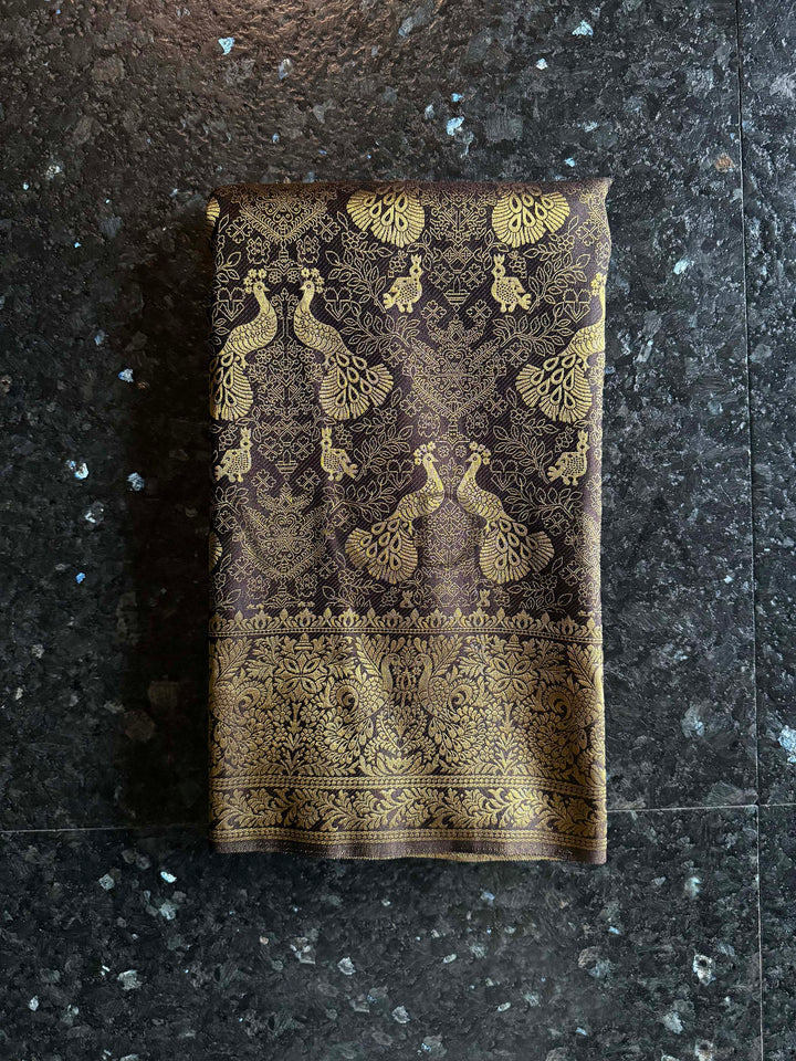 Folded fabric with gold peacock patterns on a dark stone surface Antique gold zari border featuring floral vines and Banarasi weaving patterns on Black saree. Beautifully draped black saree highlighting fine gold woven peacock motifs and a traditional diamond pattern pallu by House of Vardha.