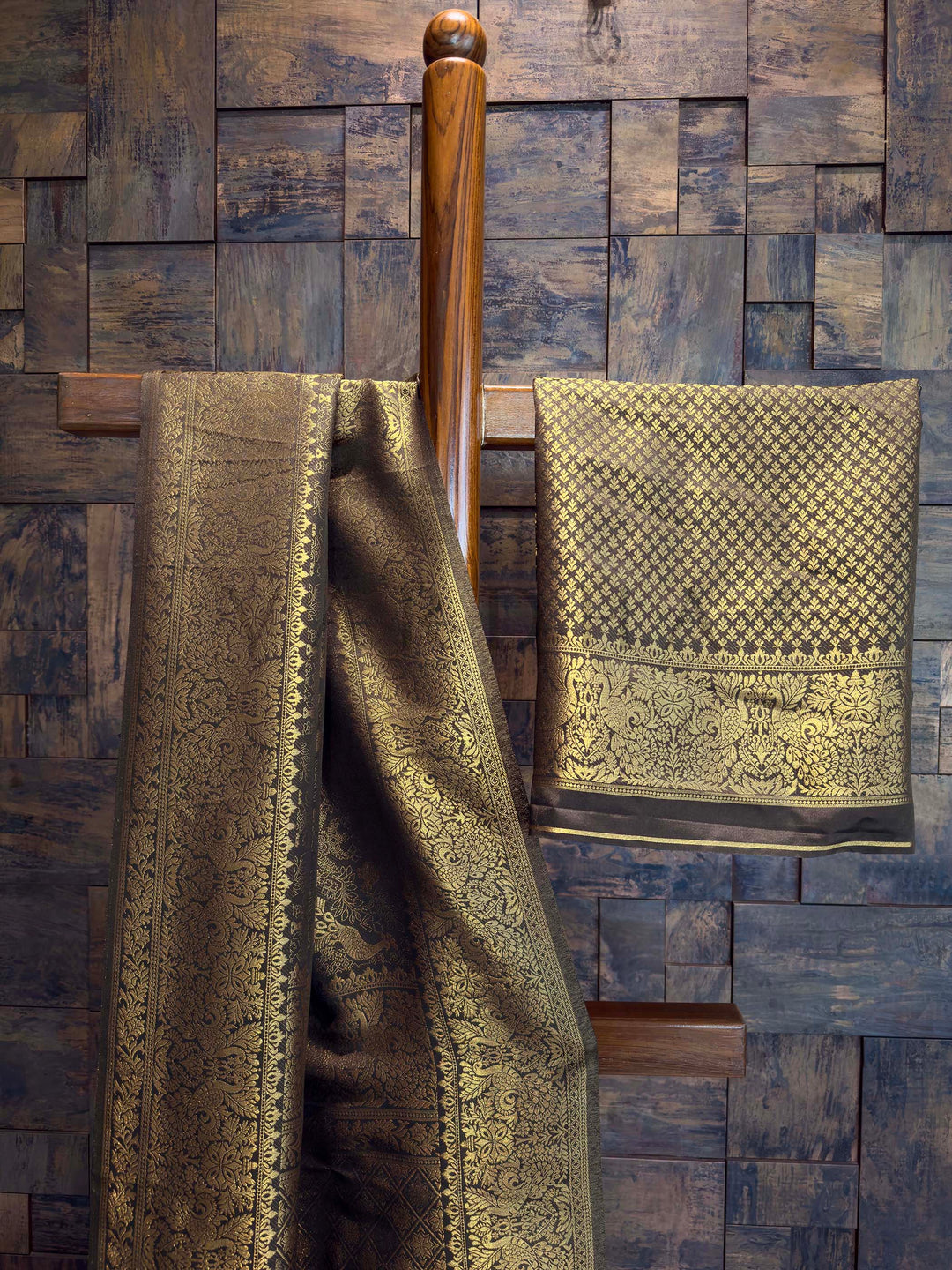 Two patterned towels hanging on a wooden towel rack against a wooden paneled wall. Art silk Black saree with dense gold zari jaal and traditional motifs displayed vertically. Authentic Indian ethnic wear featuring a striking black saree richly woven with golden threads, an exclusive House of Vardha design.